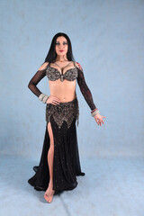 Beautiful dancer in oriental belly dance outfit on blue background in studio