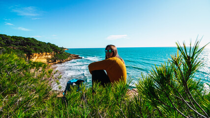 Fototapeta premium Freedom Young Girl Sitting on the Edge of Cliff hearing Wind near Blue Sea Alone. Love and Success Concept