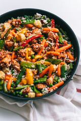 Chicken meat, rice and vegetables in a black pan on the white table.