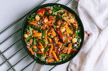 Chicken meat, rice and vegetables in a black pan on the white table.