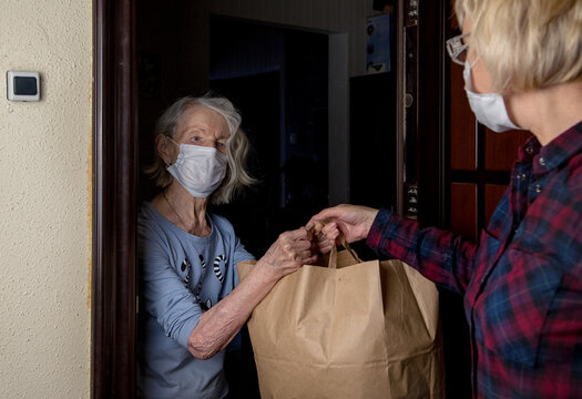 An older masked woman receives a bag of food from volunteer neighborhood help.