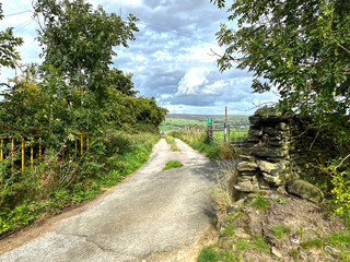 Narrow road, leading from, Thwaites Brow Road, with small trees, and distant hills in, Thwaites, Keighley, UK