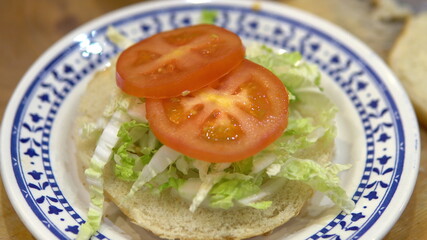 Making a burger at home. Put salad and tomatoes on the bun.