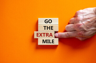 Go the extra mile symbol. Wooden blocks with words 'Go the extra mile'. Male hand. Beautiful orange background. Business and go the extra mile concept. Copy space. - obrazy, fototapety, plakaty