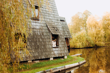 Wooden whimsical cozy house in the autumn park near the lake and a couple in love