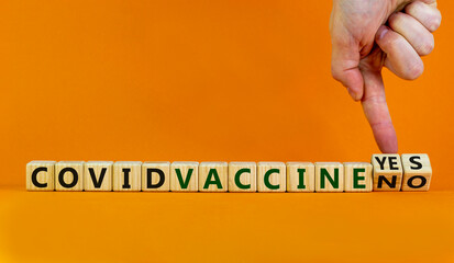 Covid vaccine yes or no symbol. Hand turns cubes and changes words 'covid vaccine no' to 'covid vaccine yes'. Beautiful orange background, copy space. Covid-19 vaccine and medical concept.