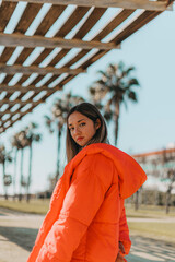 Chica joven adolescente mujer con abrigo naranja invierno con la playa de fondo y palmeras