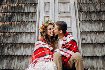 Young couple covered with a blanket kissing in front of a fabulous wooden house sitting on the stairs