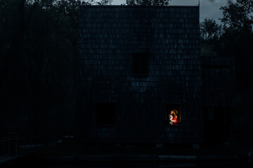 Fototapeta na wymiar A wooden house in the middle of the lake in the evening with a couple in love inside. Romantic date.