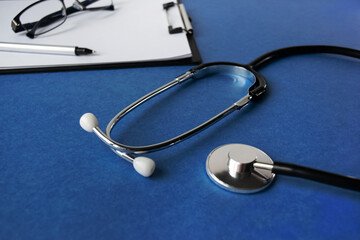 Doctor's workplace. Top view on a blue background with medical equipment - stethoscope, tablet with a blank sheet of paper, glasses. Medical concept.