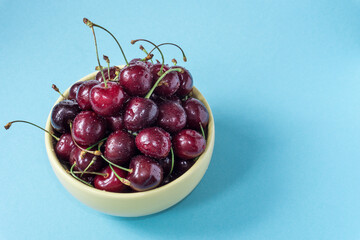 Top view of sweet cherries in a yellow bowl on a blue background. Water drops on berries.