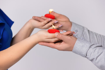 Hands of a young couple holding candles in the form of red hearts on a white background. Love and holiday concept.