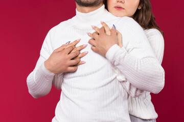 Red background. Enlarged photo of an embrace where girl's hands hug her soulmate, white sweater. Love on Valentine's Day