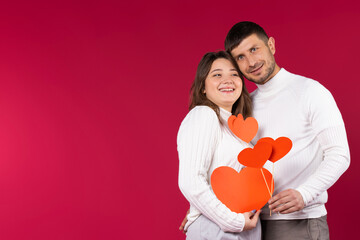 Portrait of happiest couple with red hearts over red background with empty blank space. St.Valentine's Day.