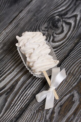 Zephyr on a stick. A ribbon bow is tied on a stick. On black pine boards.
