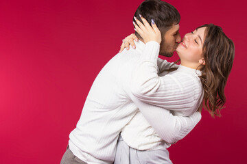 Young couple have fun hugging and fooling around on red background with blank side space.