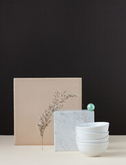 Simple abstract geometric minimalism still life with white bowls and panicle of a rush balancing upon marble on beige table on brown background, copy space, abstract design concept