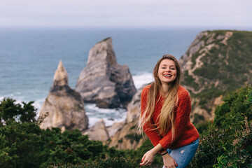 Naklejka premium Happy tourist girl standing on the edge of a cliff against the backdrop of a beautiful view of the sea and the beach.