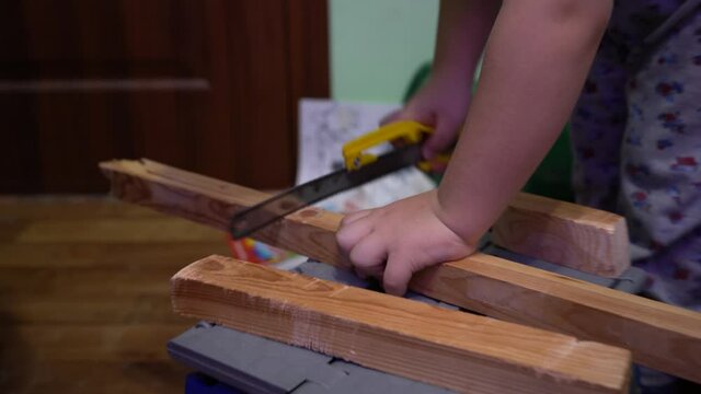 A child is sawing a wooden board with a hacksaw.