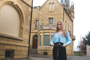 Fototapeta premium Young blonde woman moving on a e-scooter at the city.
