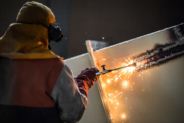 Demolition construction worker using a flame torch to cut up heavy machinery