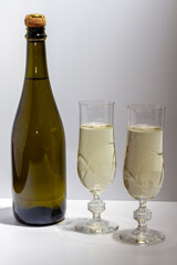 Green bottle with champagne inside and two glasses with champagne on a white background.