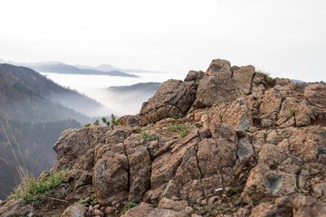 Rough rock on a mountain top with a view to hills that are peeking through clouds