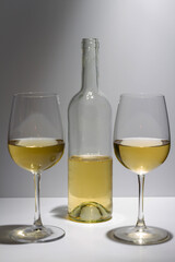 Transparent bottle with white wine inside and two glasses with white wine on a white background.