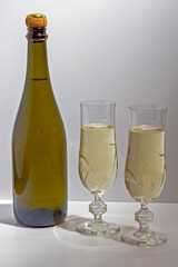 Green bottle with champagne inside and two glasses with champagne on a white background.