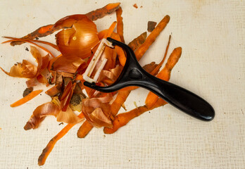 onion peel and carrot peel on a board with a peeler