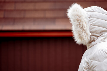 Side view of a female wearing a beige puffer jacket with its hood on her head covering her face © Ben White/Wirestock