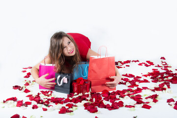 woman holds and hugs with admiration paper shopping bags among red rose petals on a white background. Valentine's Day gifts. Shopping for Valentine's Day.
