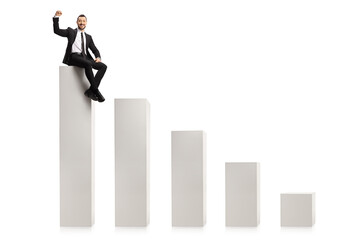 Obraz premium Professional man sitting on the highest column of a bar chart and gesturing a win sign