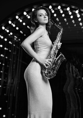 Gorgeous brunette model woman in elegant dress with saxophone