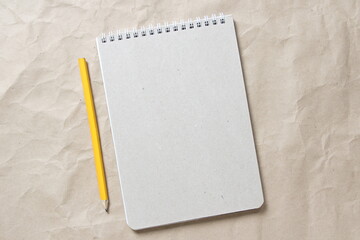 Gray notepad with white coiled spring and pencil on a background of beige crumpled craft paper. With empty space for text and design