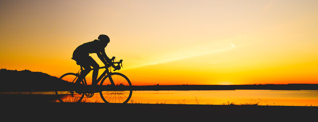 Unrecognizable silhouette man riding bicycle against sunset sky. Road biking cyclist workout,...