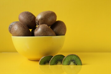 Still life fruit in a yellow bowl plate on a yellow background next to lies a piece of kiwi illuminatiited yellow trend color copyspace