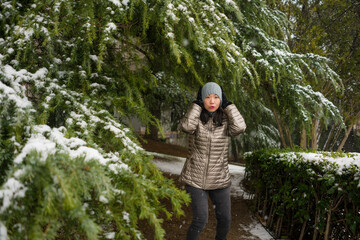 lifestyle portrait of  young happy and attractive Asian Korean woman in winter hat and mask at beautiful city park playing with snow cheerful enjoying cold Christmas holidays