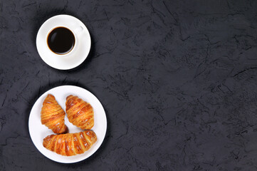 A cup of hot coffee and croissants on a black background. Breakfast with coffee and fresh pastry. Fresh cake and pastry. Flat lay. Copy space. Place for text.Top view. Food.