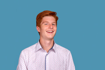 Studio shot of smiling red head young boy against blue background