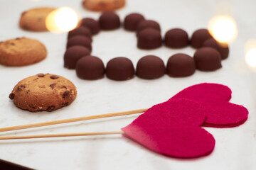 Valentine's Day. Heart made of chocolates and cookies on a white background with lights