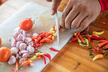 close up of a hand cutting white onions and chilli pepper on a kitchen board with a knife