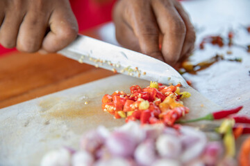 close up of a hand cutting white onions and chilli pepper on a kitchen board with a knife