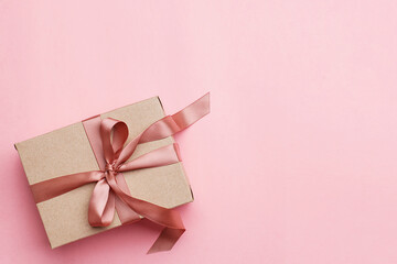 Cardboard gift box tied with a pink satin ribbon on pink background. Overhead view, copy space....