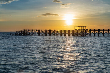 silhouette of a wooden jetty at sunset with blue soft waves in the fore ground