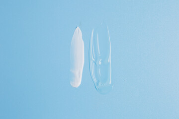 drops of white face cream and clear body gel smeared on a blue background