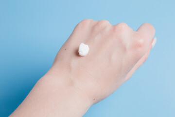 drop of white body cream on the girl's hand on a blue background