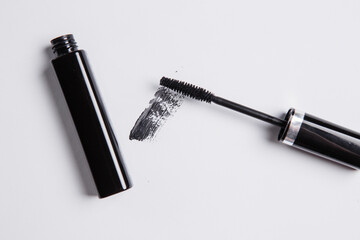 Fototapeta premium smear of black mascara is smeared on a white background, an applicator brush and a tube of black lie next to the smear of mascara