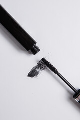 smear of black mascara is smeared on a white background, an applicator brush and a tube of black lie next to the smear of mascara