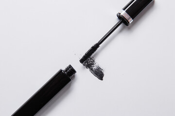 smear of black mascara is smeared on a white background, an applicator brush and a tube of black lie next to the smear of mascara